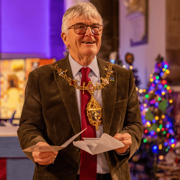 A smiling man is stood facing the church congregation holding a christmas card.