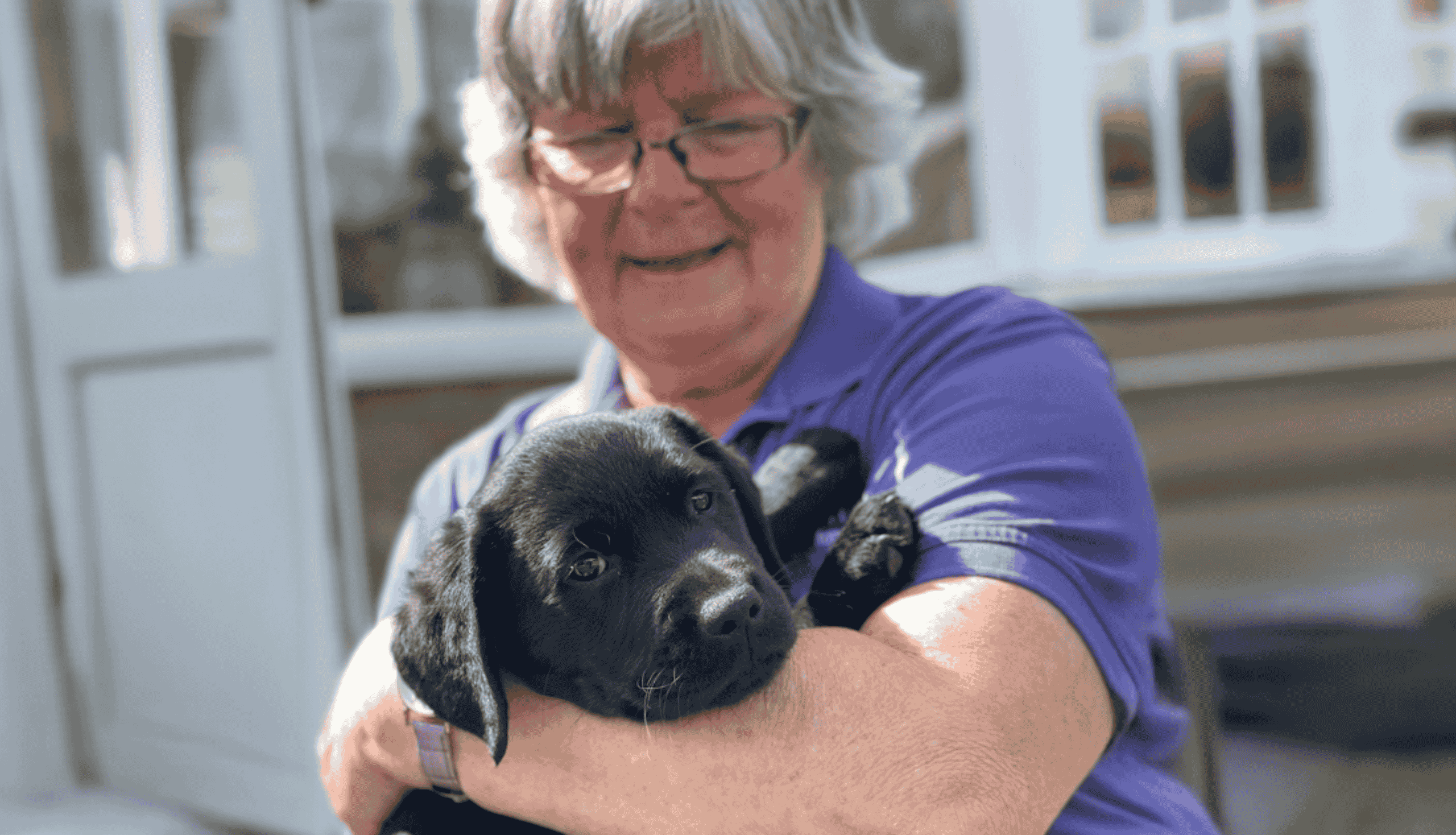 Puppy Training volunteer holding black lab pup in her arms